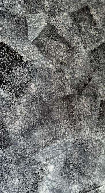 A grey and black spray-and-block-printed surface with a crackled texture.