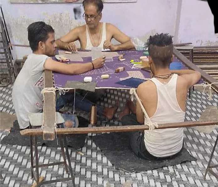 Three embroiderers working around a frame of purple fabric.