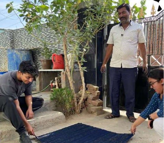 Three people with a length of indigo cloth laid out to dry in a courtyard.