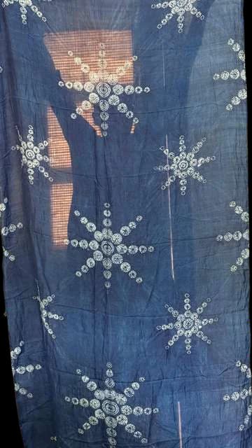 Indigo cloth with white star-burst resist motifs, held up to a window.