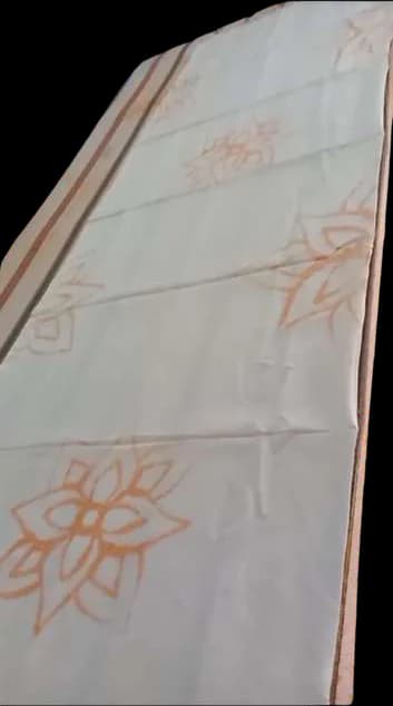 An orange stitched flower outline on white cloth.