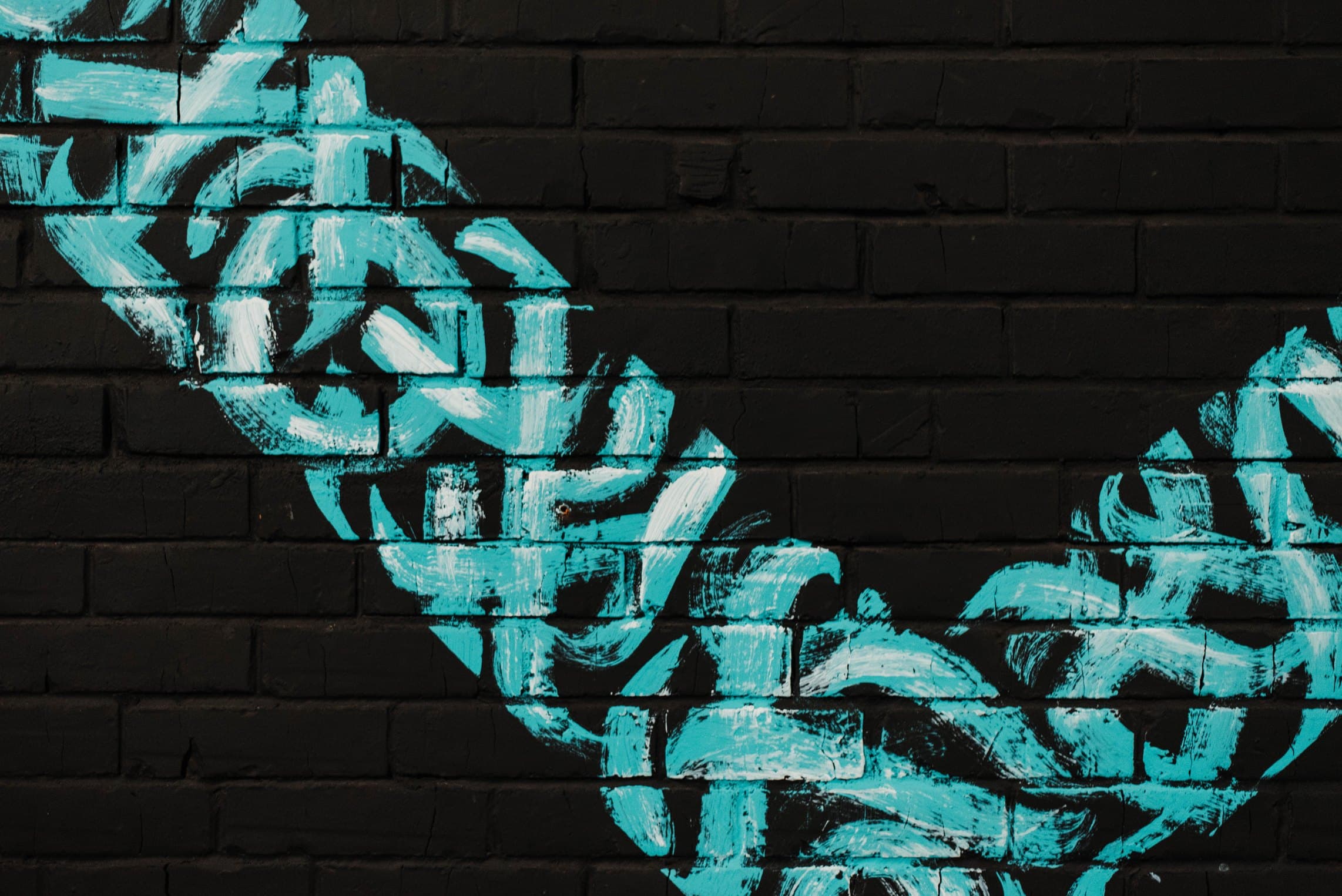 Teal graffiti brushed across a black-painted brick wall.